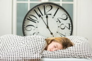 Woman asleep in bed with big clock behind her