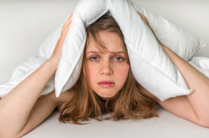 Woman in bed covering ears with pillow because of noise